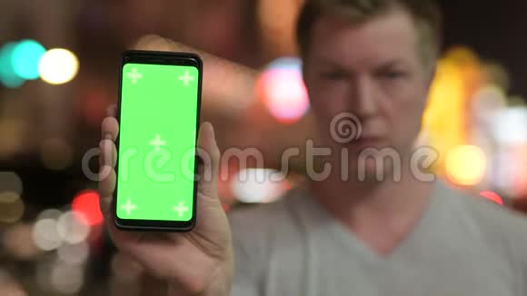 年轻快乐的游客晚上在唐人街用绿色屏幕显示电话视频的预览图