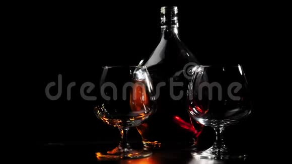 豪华白兰地圆瓶的金色干邑和两个玻璃杯旋转在一张木桌上玻璃在灯光下眩光布兰迪视频的预览图