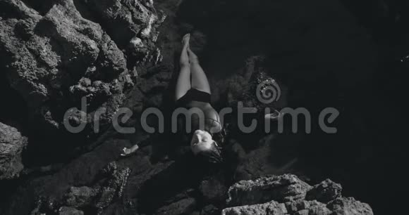 黑白镜头雌性自由战士躺在靠近海洋的岩石上拍摄于12位彩色电影摄影机视频的预览图