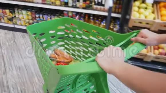 通过超市的过道可以看到女性移动购物车里面有新鲜的五颜六色的蔬菜和水果视频的预览图