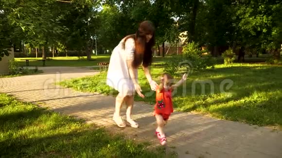 婴儿和她的母亲一起迈出第一步跪倒在她的膝盖上沿着公园的行走慢动作视频的预览图