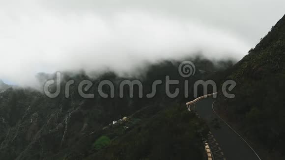 静态鸟瞰巨大的云在一条没有汽车的孤独道路上飞得很低在山脊上蜿蜒的高高特内利夫视频的预览图