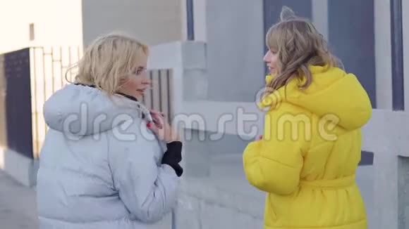 两个女朋友在寒冷和阳光明媚的秋日街头散步聊天和闲聊后景视频的预览图