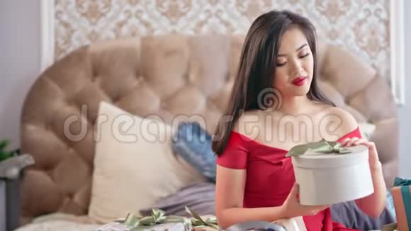 迷人的亚洲年轻女子穿着豪华红色连衣裙打开礼品盒微笑着视频的预览图