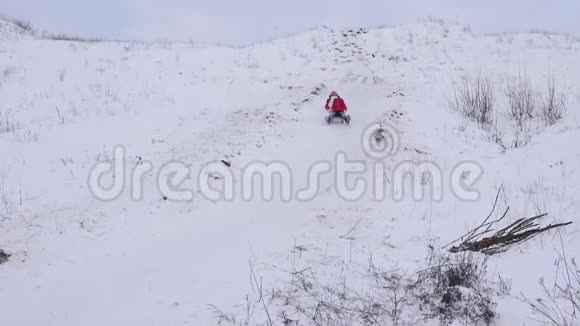 快乐的孩子在雪中滑下山笑雪飞到女孩面前公园里的圣诞节假期视频的预览图