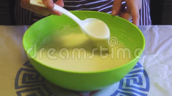 在家庭厨房里一只雌性手在绿色的碗里用一个面糊和一个白色的塑料勺子混合着一个面糊视频的预览图