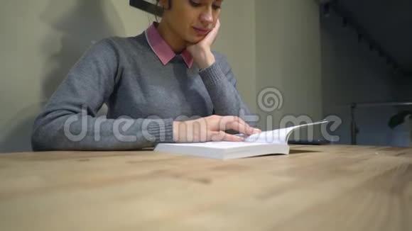年轻的黑发女孩坐在桌旁看书视频的预览图