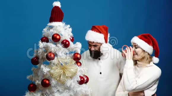 可爱的一对幸福的夫妇在圣诞树旁迎接新年一对年轻夫妇戴着新年帽子装饰圣诞节视频的预览图