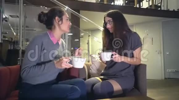 坐在椅子上两个浅黑肤色的年轻女孩微笑着聊天喝茶视频的预览图