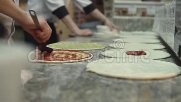 一群穿制服的厨师把番茄酱均匀地放在比萨饼面团圈上视频的预览图