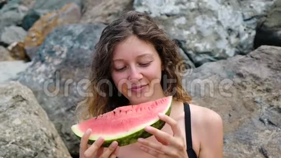 一个年轻漂亮的卷发女人咬掉西瓜的肖像慢动作视频的预览图