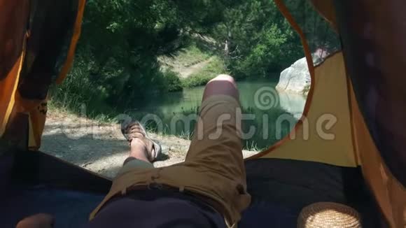 一个年轻人腿躺在帐篷里徒步旅行一天后休息一个人躺在靠近绿色森林的帐篷里视频的预览图