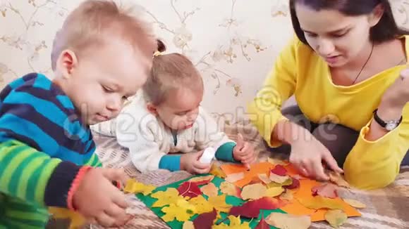 带着孩子的年轻妈妈从秋天的叶子里做秋天的贴花带着妈妈的小女孩在秋天的秋天视频的预览图