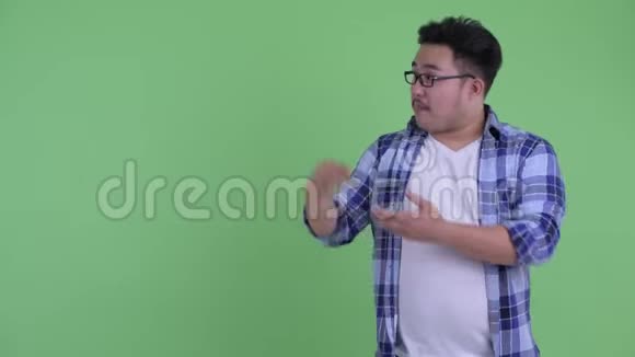 快乐年轻体重超重的亚洲时髦男人一边说话一边展示自己视频的预览图