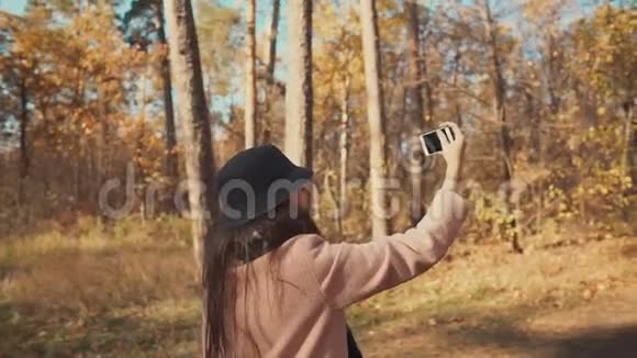 年轻的博主女孩在秋天的森林散步时通过电话拍摄自己视频的预览图