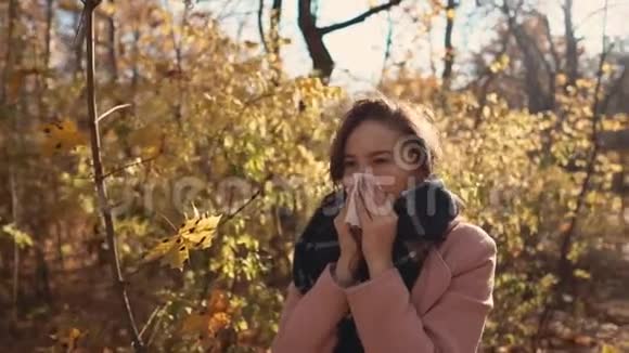 秋日年轻的病妇站在公园里打喷嚏用手帕视频的预览图