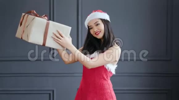 微笑亚洲女性圣诞老人拿着大纸箱礼品盒在灰色背景的工作室鞠躬视频的预览图