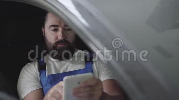专业机械师坐在车里核实他手机上的信息穿制服的胡子男视频的预览图