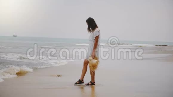 年轻美丽快乐的白种人女人穿着白色的夏装在田园诗般的热带海洋海滩上抚摸着温暖的波浪视频的预览图