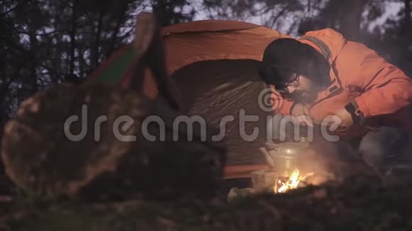 黄昏时分一位游客在帐篷的背景下点燃森林里的火温暖水壶里的水这就是视频的预览图