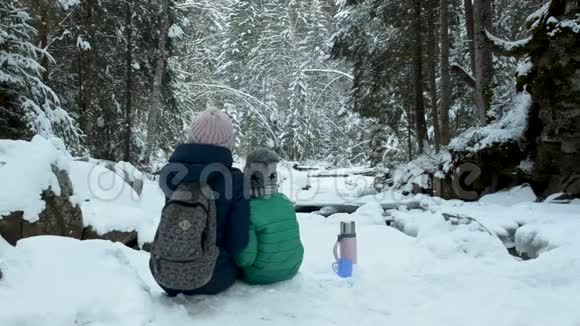 妈妈和儿子坐在一起拥抱在白雪覆盖的森林里冬季阴天后景视频的预览图