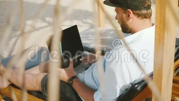 背景镜头集中成功的男性自由职业者与饮料使用笔记本电脑在休闲椅在夏季海滩度假村视频的预览图