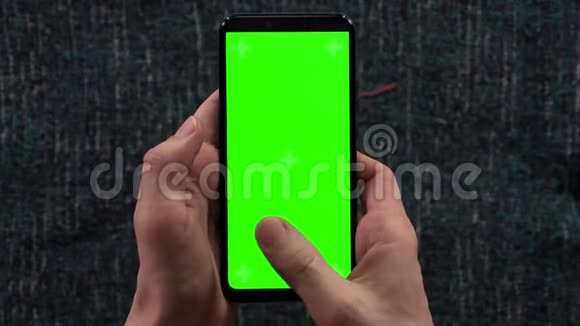男人的特写镜头双手拿着智能手机背景衣柜里有一个水平的绿色屏幕准备着衣服视频的预览图