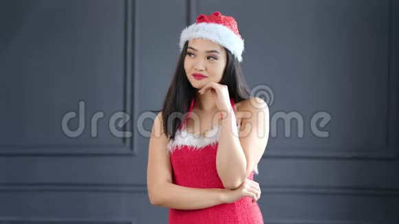 穿着圣诞老人套装的漂亮的亚洲女人微笑着在画室里摆着灰色背景视频的预览图