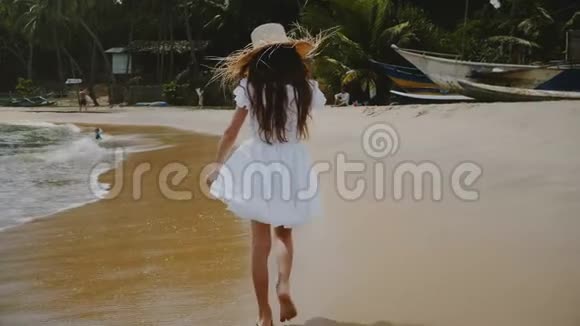 镜头倾斜着快乐的小女孩走在美丽的热带海洋海滩上戴着大草帽视频的预览图
