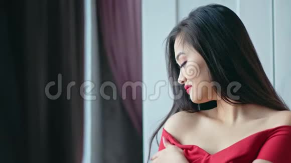 中等特写美丽的亚洲女人穿着红色连衣裙微笑着看着窗户视频的预览图