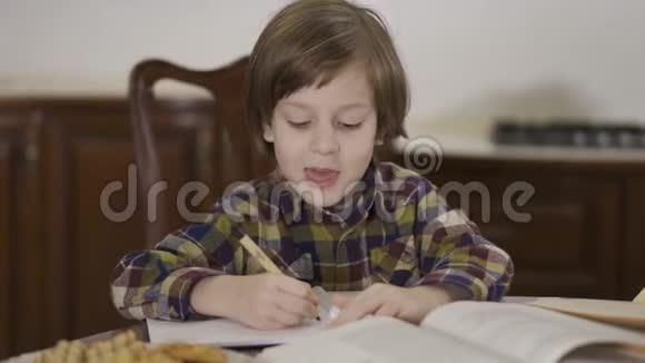 可爱有趣的小男孩穿着格子衬衫坐在家里的桌子旁做作业他的学生在画视频的预览图