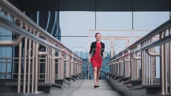 自信的商务女性穿着红色连衣裙走在现代建筑的背景下一位年轻女子的肖像视频的预览图
