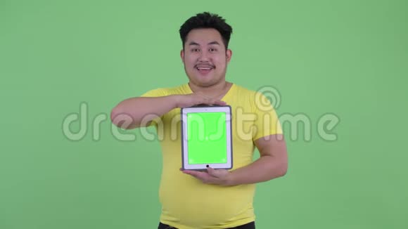 快乐年轻体重超重的亚洲男人在看数字平板电脑视频的预览图