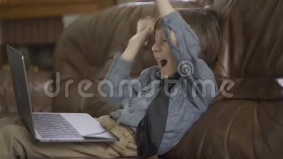 肖像可爱的小男孩坐在皮革沙发上腿上有笔记本电脑在空中扔钱视频的预览图