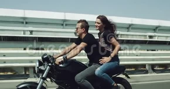 在夏天刮风的日子里年轻夫妇骑着一辆黑色的大摩托车在高速公路上兜风女士高兴地享受着视频的预览图