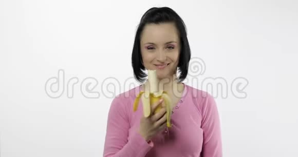 年轻的美女在白色背景下吃大而新鲜的香蕉视频的预览图