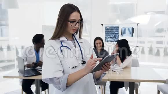 英俊的年轻女子在诊所的背景上使用带有考克的平板电脑视频的预览图