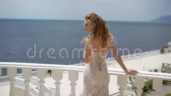 年轻的新娘站在阳台上摆姿势海边的婚礼视频的预览图