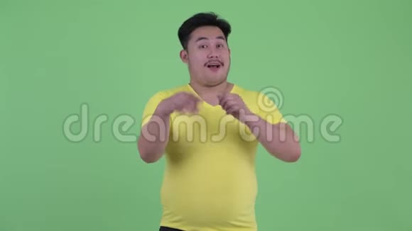 一个困惑的超重的亚洲年轻人在竖起大拇指和竖起大拇指之间做出选择视频的预览图