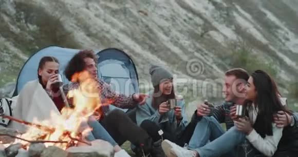 茶时间为同一群不同种族的朋友晚上露营中间篝火4k视频的预览图