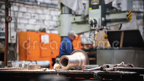 桌子上的工厂里面有金属零件和工具在背景中一个人在机床上工作视频的预览图