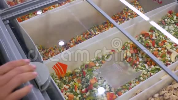 一个年轻的女人在超市里选择了一种绿色的冷冻蔬菜视频的预览图