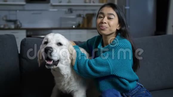 年轻的印度妇女在沙发上抚摸和拥抱狗视频的预览图