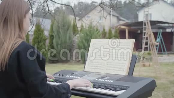 专业可爱的钢琴家在后院的合成器上演奏古典钢琴音乐真人系列视频的预览图