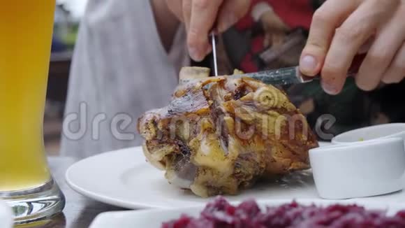 人手拿刀叉切一个猪肉指节放在盘子上附近有一杯啤酒视频的预览图