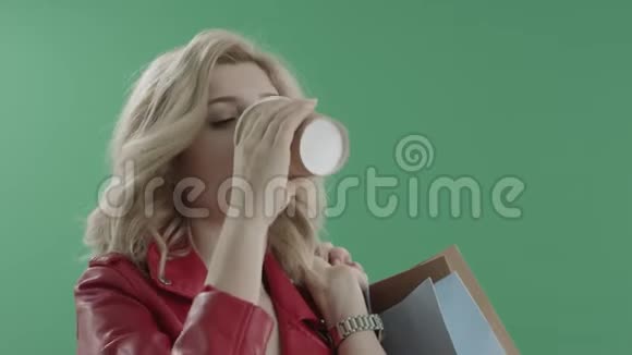 穿红色夹克的女人喝着咖啡手里拿着袋子对着绿色的屏幕视频的预览图