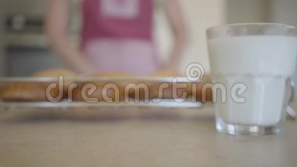 背景上的桌子上有两杯牛奶一个年轻的女人和刚从烤箱里烤出来的面包关门视频的预览图
