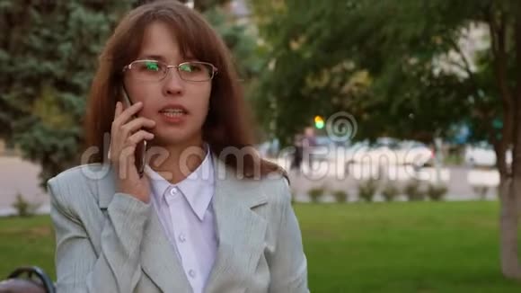 女人在智能手机上说话在公园里喝咖啡戴眼镜的女商人穿着轻便西装上班视频的预览图