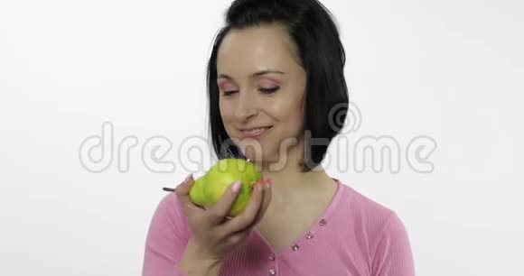 年轻漂亮的女人在白色背景上吃着大而多汁的绿梨视频的预览图