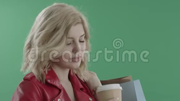穿着红色夹克的漂亮女人喝着咖啡手里拿着袋子对着绿色的屏幕视频的预览图
